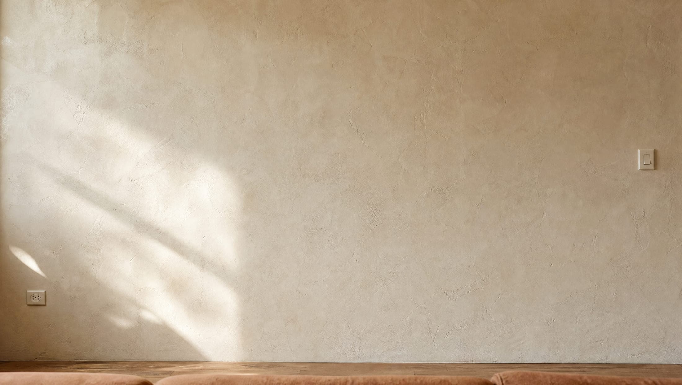 A bare plaster wall with a socket at the lower left and a light switch at the right